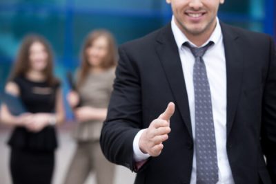 Confident young business man offering hand for greeting or agreement handshake outdoor. Successful Deal Concept. Businesspeople Team on the background. Close-up